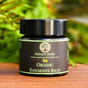Container of Nature Body Kawakawa Balm 30g on a wood table with some greenery behind it.