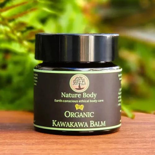 Container of Nature Body Kawakawa Balm 30g on a wood table with some greenery behind it.