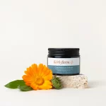 HerbFarm Calendula Cream 50ml on a stone next to a calendula flower.
