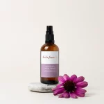 HerbFarm Renew Refine Facial Toner 100ml spray bottle sitting on a rock next to a purple flower