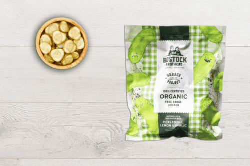 A bag of Bostock Butterfly Chicken Dill Lemon on a table with a bowl of pickles next to it.