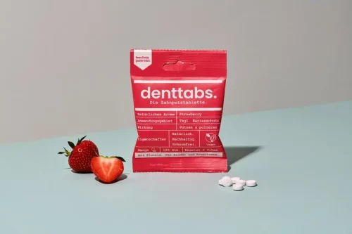 Denttabs Tooth Tablets Strawberry in its packaging next to strawberries and some loose tablets