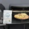 OrganicDough Pizza Dough Ball cooked in front of a pizza oven, next to its packaging