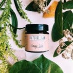 a jar of NaturallyTrish Fungus Salve on a table surrounded by plants and herbs