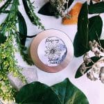 a jar of NaturallyTrish Helping Hand Salve on a table surrounded by plants and herbs